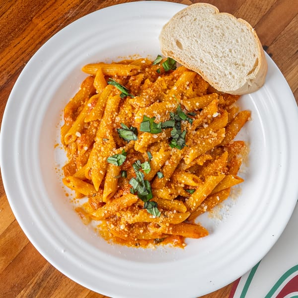 Penne pasta in a creamy red sauce, topped with fresh basil and grated cheese, served with bread.
