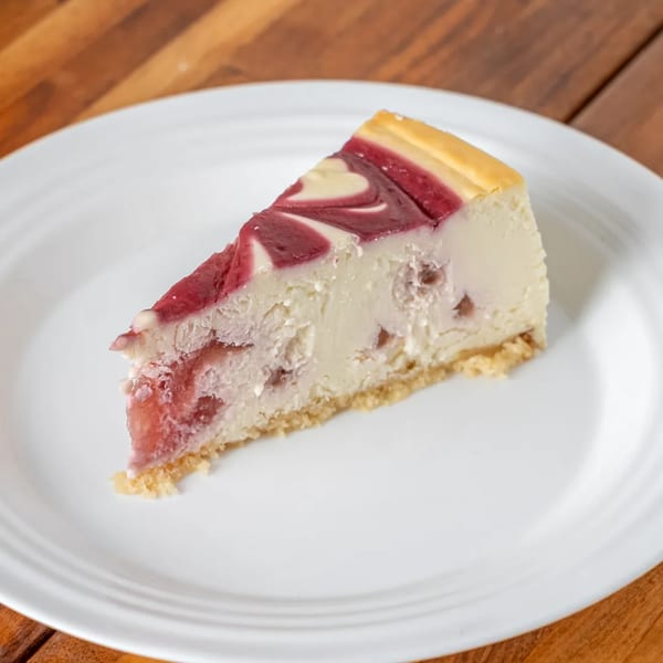 A slice of P&M Fine Foods cheesecake with a red swirled topping on a white plate.