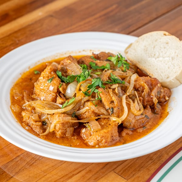 P&M Fine Foods' chicken cacciatore with onions and parsley, served with a slice of bread.