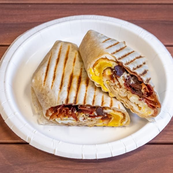 Two grilled breakfast wraps, filled with scrambled eggs, bacon, and cheese, on a white paper plate.
