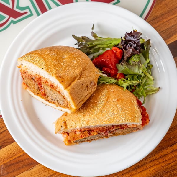 P&M Fine Foods' meatball sub, cut in half, with a side of green salad and roasted red peppers.