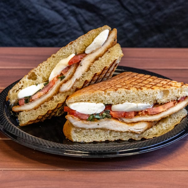 Two halves of a grilled chicken panini with mozzarella, tomatoes, and basil on a black plate.