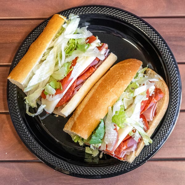 Two P&M Fine Foods deli subs, packed with meat, cheese, and lettuce, on a black plate.