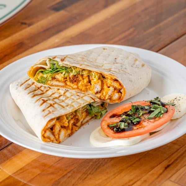 P&M Fine Foods' buffalo chicken wrap, cut in half, with a side of caprese salad on a white plate.