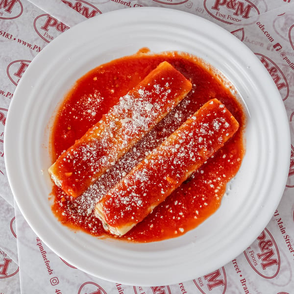Two cheese manicotti covered in red sauce and grated cheese on a white plate from P&M Fine Foods.