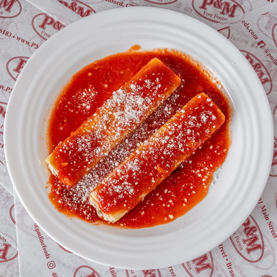 Two cheese manicotti covered in red sauce and grated cheese on a white plate from P&M Fine Foods.