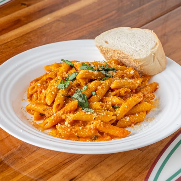 Penne pasta in a creamy tomato sauce, topped with fresh basil and grated cheese, served with bread.