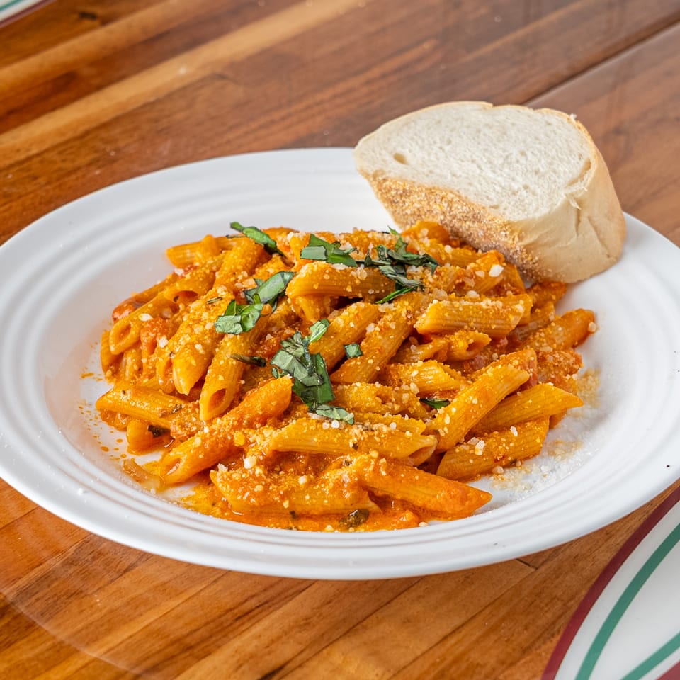 Penne pasta in a creamy tomato sauce, topped with fresh basil and grated cheese, served with bread.