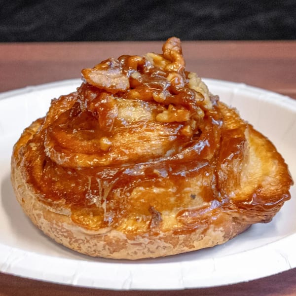 A sticky bun with nuts and caramel glaze on a white paper plate from P&M Fine Foods.