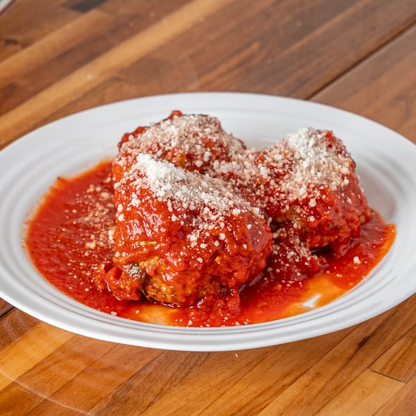P&M Fine Foods' meatballs in rich red sauce, topped with grated Parmesan cheese on a white plate.