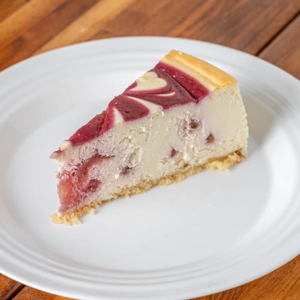 A slice of P&M Fine Foods cheesecake with a swirled raspberry topping on a white plate.