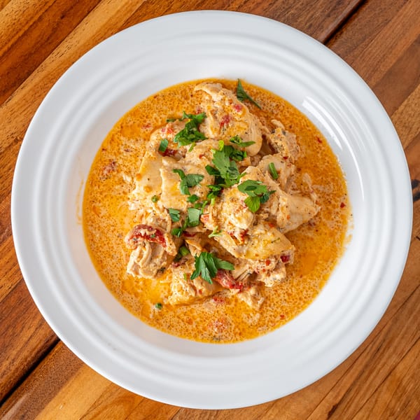 P&M Fine Foods' creamy chicken dish with sun-dried tomatoes and fresh parsley in a white bowl.