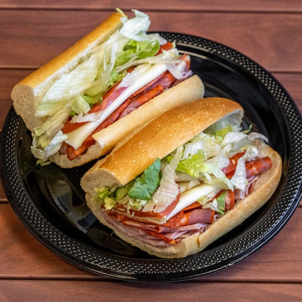 Two P&M Fine Foods deli subs with meat, cheese, lettuce, and tomatoes on a black plate.