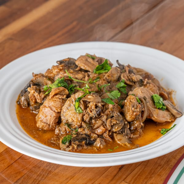 Steaming hot P&M Fine Foods chicken and mushrooms in a rich brown sauce, garnished with fresh parsley.