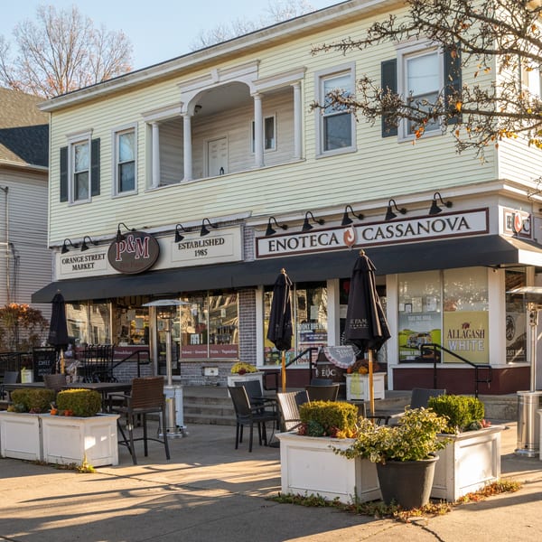 Exterior of P&M Fine Foods deli with outdoor seating, umbrellas, and planters under a light yellow building.