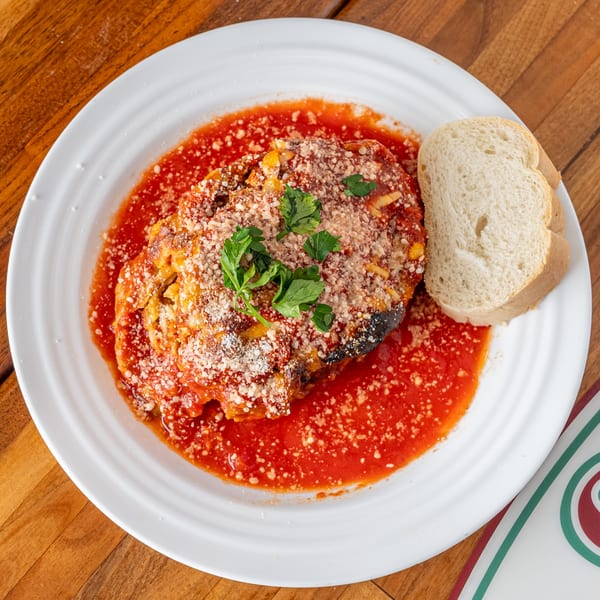 Eggplant Parmesan with tomato sauce, grated cheese, parsley, and a side of bread.