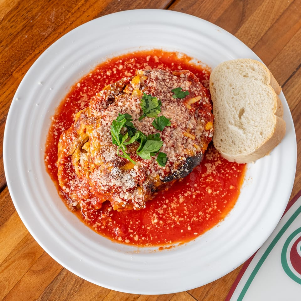 Eggplant Parmesan with tomato sauce, grated cheese, parsley, and a side of bread.
