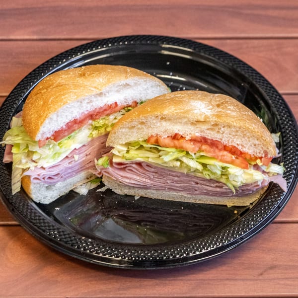 A P&M Fine Foods deli sandwich, cut in half, with ham, lettuce, and tomato on a black plate.