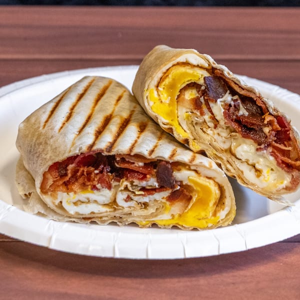 Two halves of a grilled breakfast wrap filled with scrambled eggs, cheese, and crispy bacon.