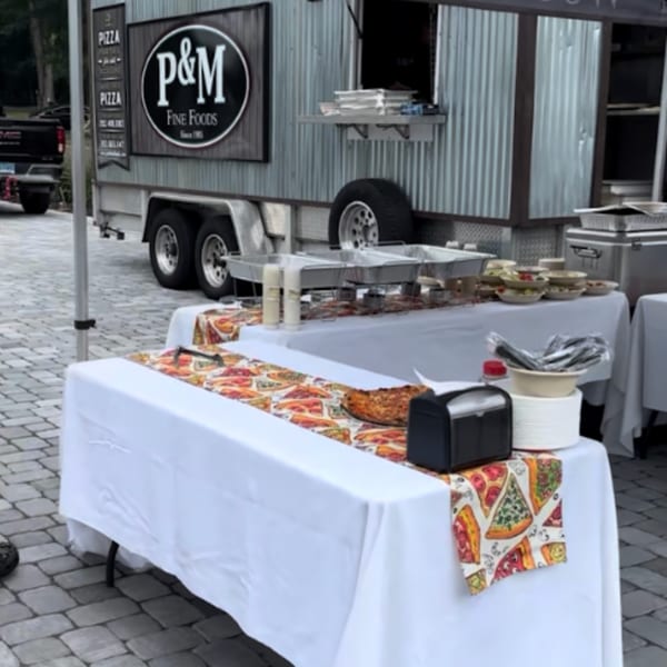P&M Fine Foods food truck with buffet tables of pizza and deli items set up outdoors.
