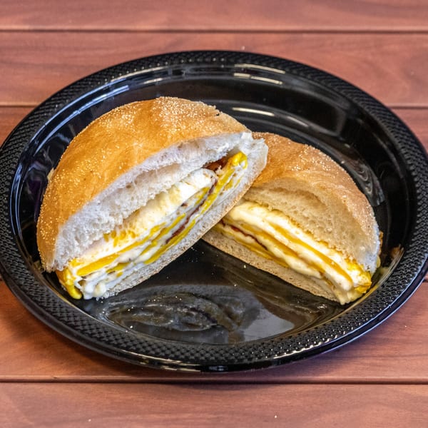 P&M Fine Foods deli sandwich, cut in half, with egg, cheese, and bacon on a black plate.